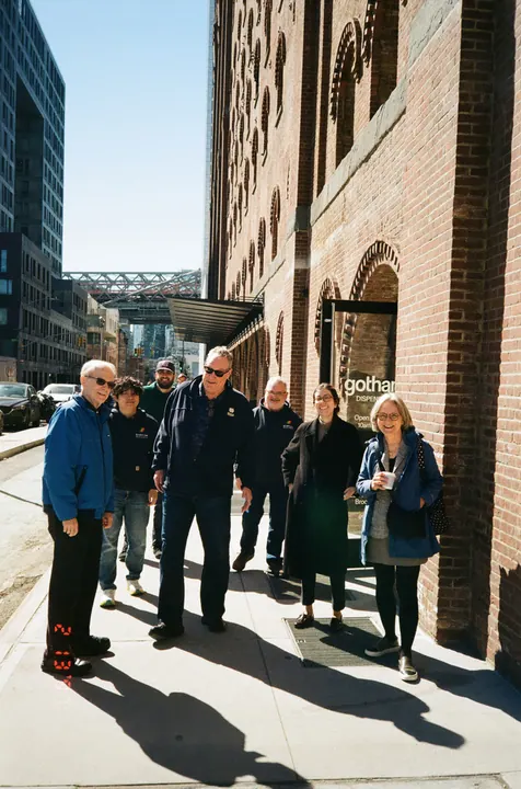 Team members pose together on a sunny sidewalk beside a brick building.