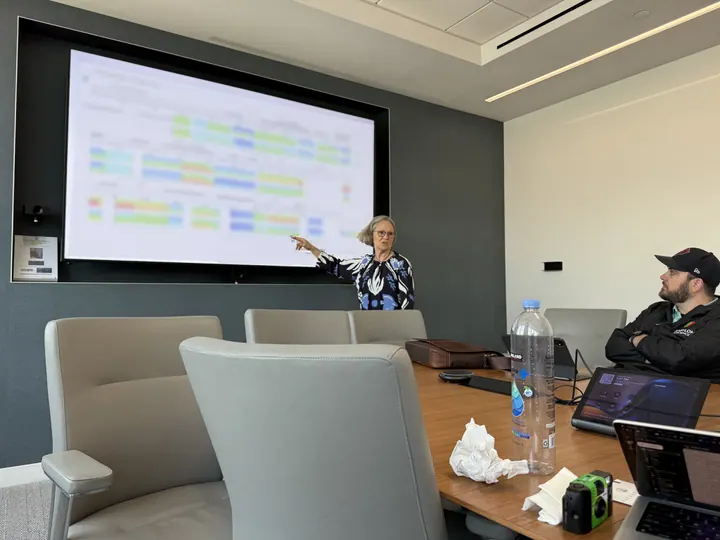 A team member points to a presentation on a large screen during a meeting.