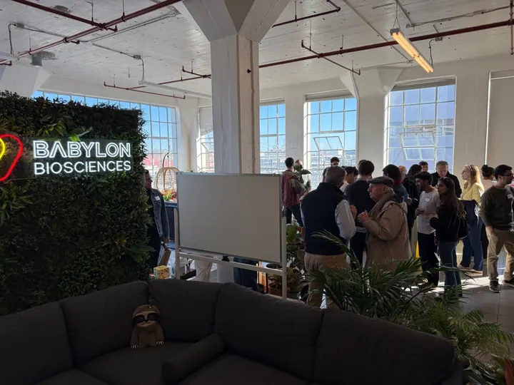People gather in the office beside an illuminated Babylon Biosciences sign.