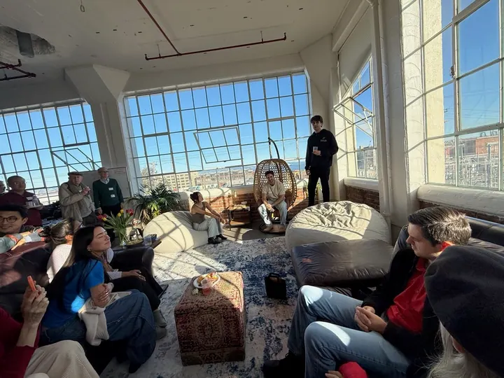People gather for a conversation in the office lounge beside large windows.