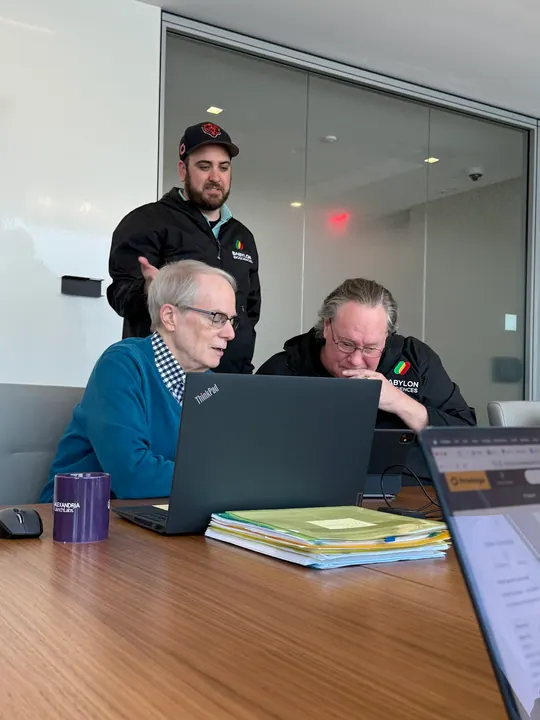 Three team members review a laptop together at a conference table.
