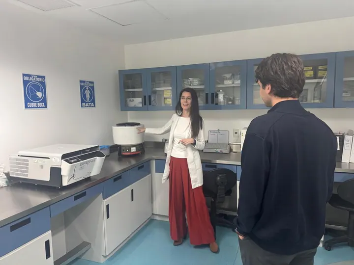 A visitor listens as a woman in a lab coat demonstrates laboratory equipment.